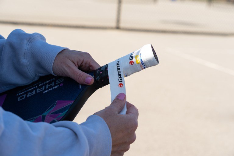 Close up image of a pickleball player replacing the grip on their paddle using Gamma overgrip
