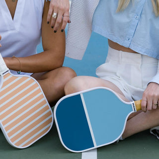 Two women sitting on pickleball court with GAMMA pickleball paddles